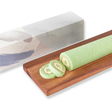 Green roll cake with two slices on a wooden tray, with a decorative box in the background.